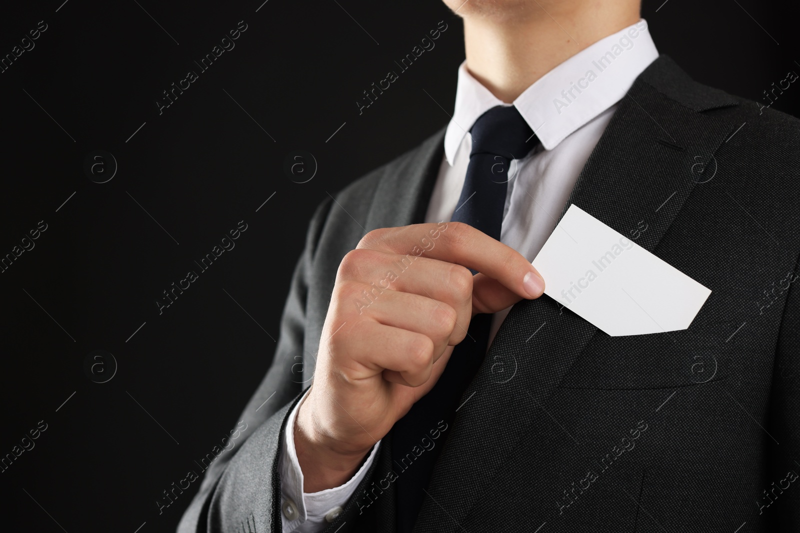 Photo of Man taking blank business card from pocket of his jacket on black background, closeup. Mockup for design