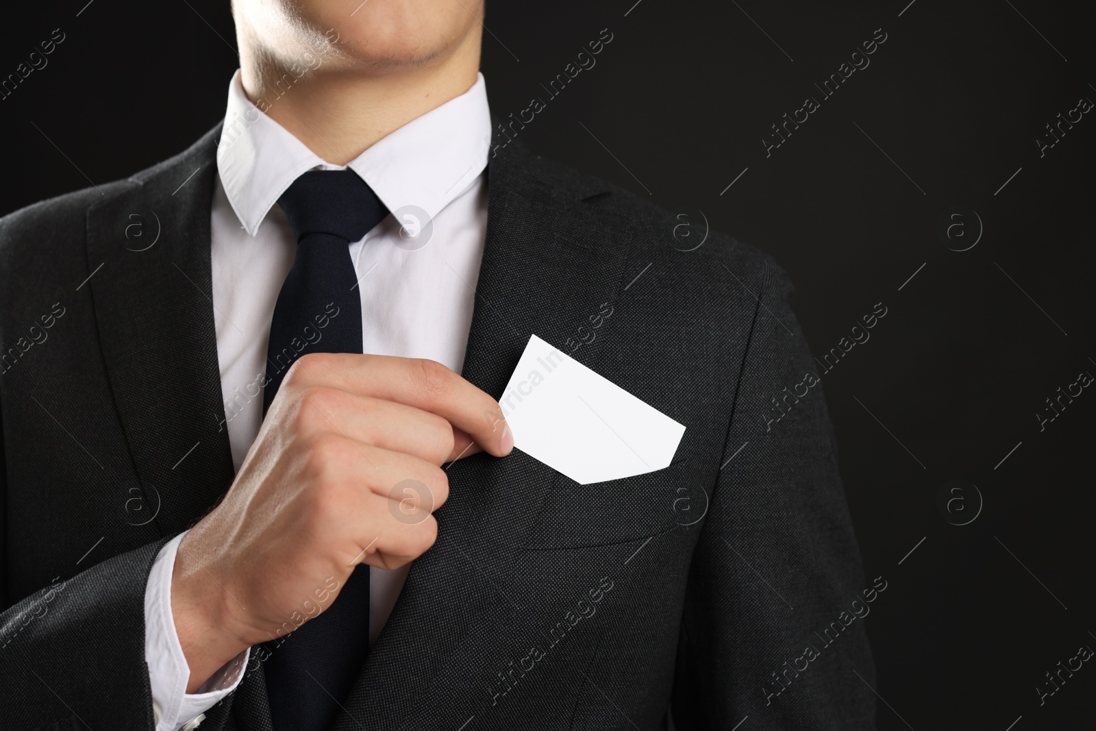 Photo of Man taking blank business card from pocket of his jacket on black background, closeup. Mockup for design