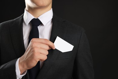 Man taking blank business card from pocket of his jacket on black background, closeup. Mockup for design