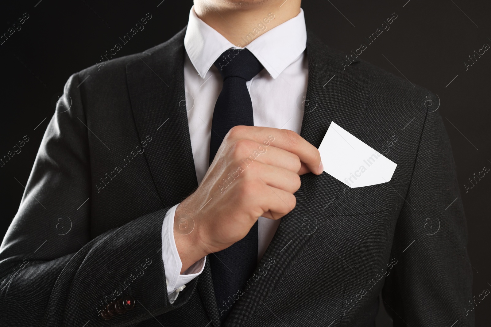 Photo of Man taking blank business card from pocket of his jacket on black background, closeup. Mockup for design