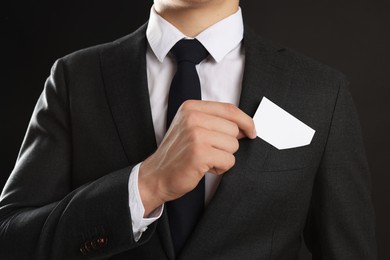 Man taking blank business card from pocket of his jacket on black background, closeup. Mockup for design