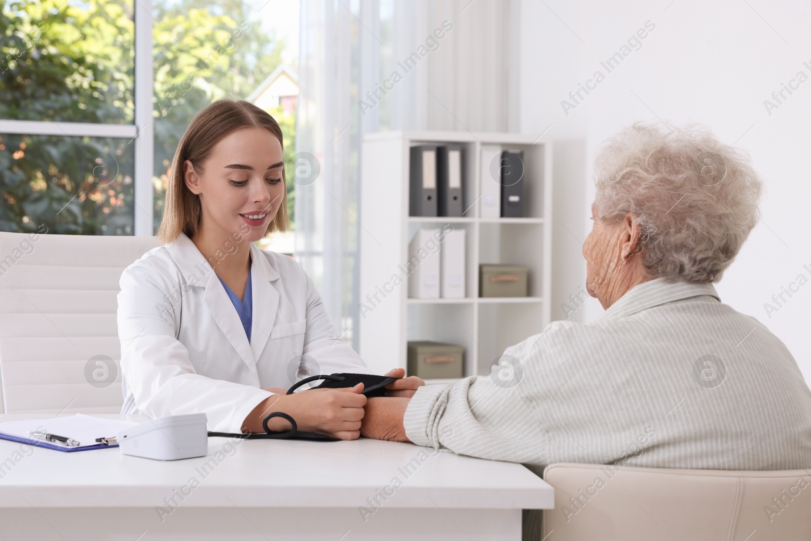 Photo of Doctor measuring patient's blood pressure at table in hospital