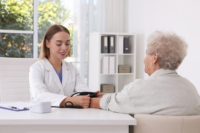 Photo of Doctor measuring patient's blood pressure at table in hospital