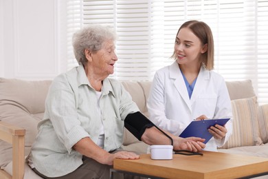 Senior woman measuring blood pressure while doctor taking notes indoors