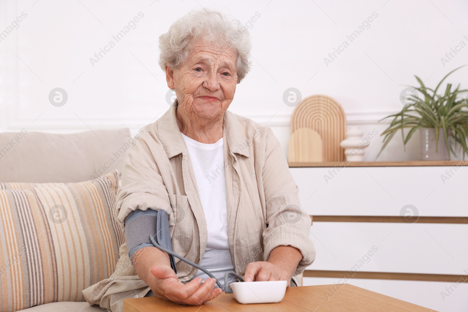 Photo of Senior woman measuring blood pressure at wooden table indoors