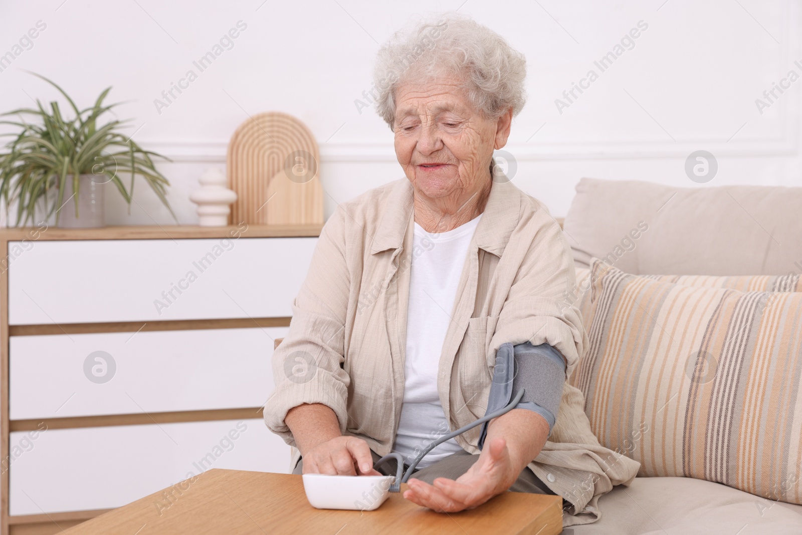 Photo of Senior woman measuring blood pressure at wooden table indoors