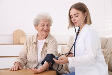 Doctor measuring patient's blood pressure at wooden table indoors