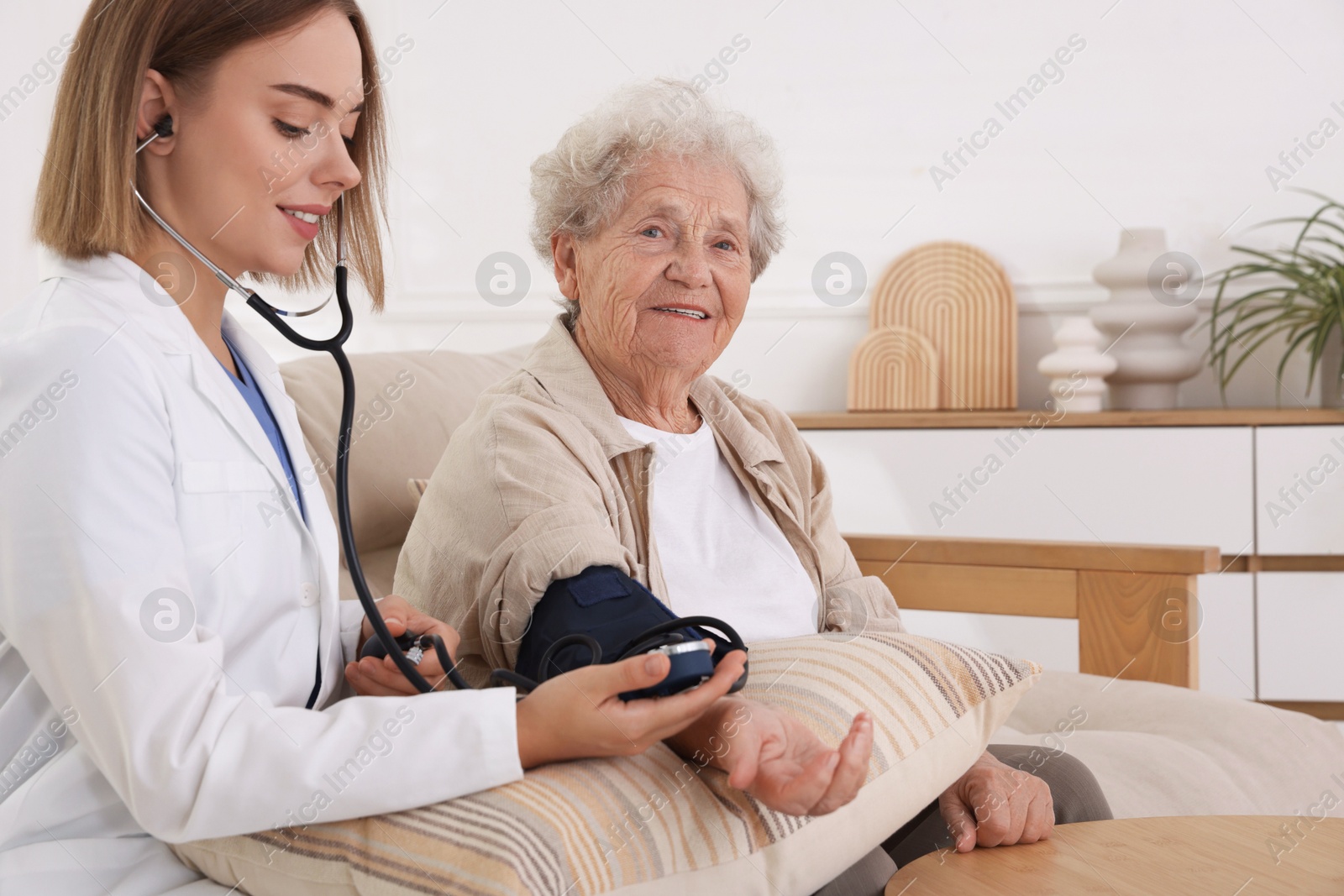 Photo of Doctor measuring patient's blood pressure on sofa indoors