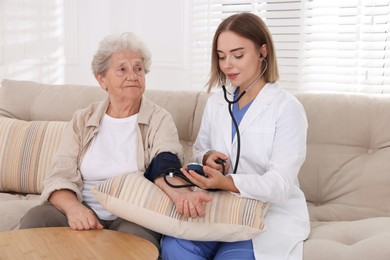 Photo of Doctor measuring patient's blood pressure on sofa indoors