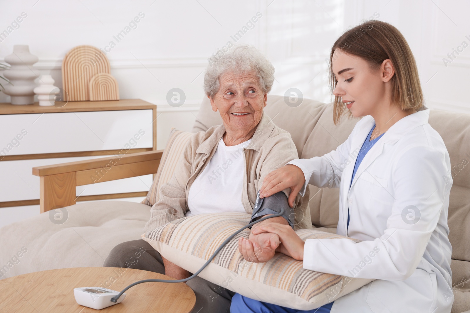 Photo of Doctor measuring patient's blood pressure on sofa indoors