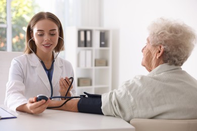 Doctor measuring patient's blood pressure at table in hospital