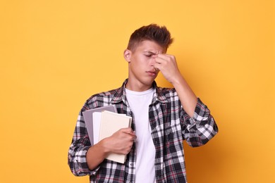 Young student with books having stress before exam on yellow background