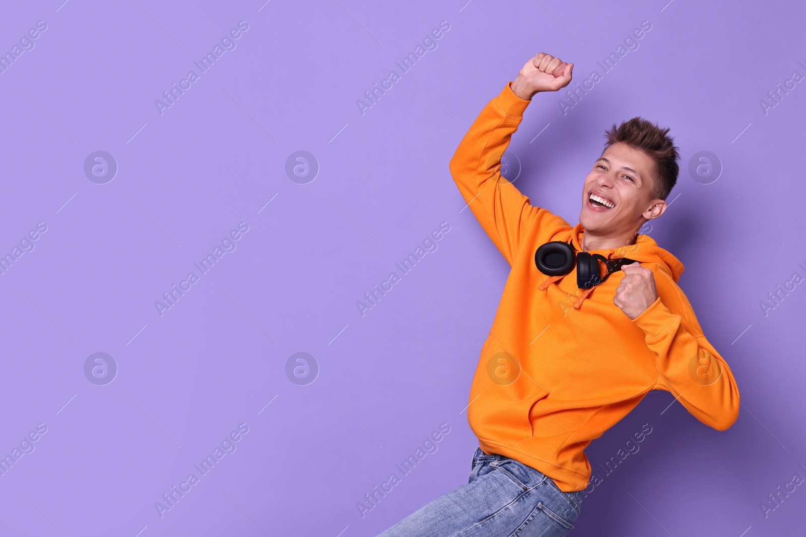 Photo of Happy young student with headphones on violet background, space for text