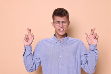 Photo of Emotional young student crossing fingers on beige background. Hope for good exam result