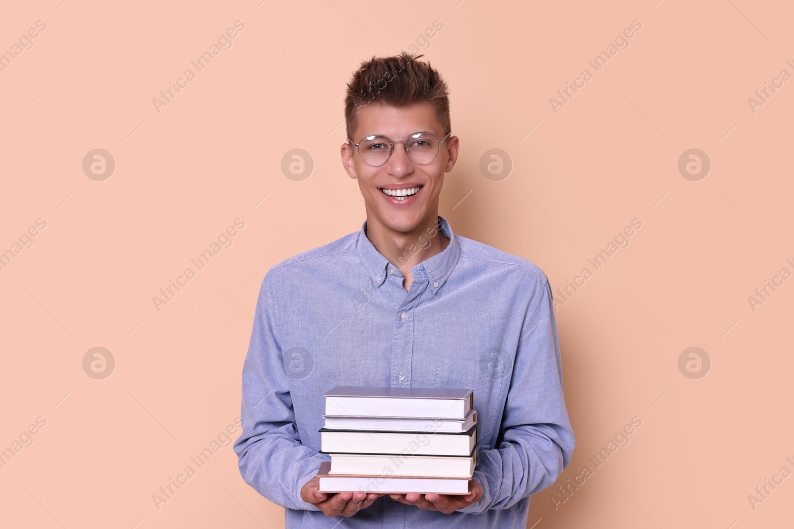 Photo of Young student with stack of books happy about his good exam result on beige background