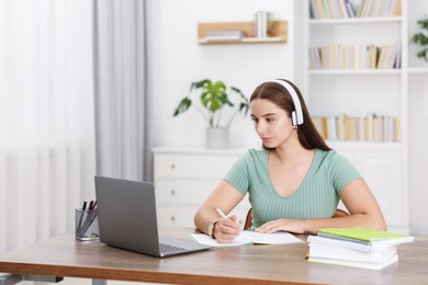 Student in headphones studying at wooden table indoors