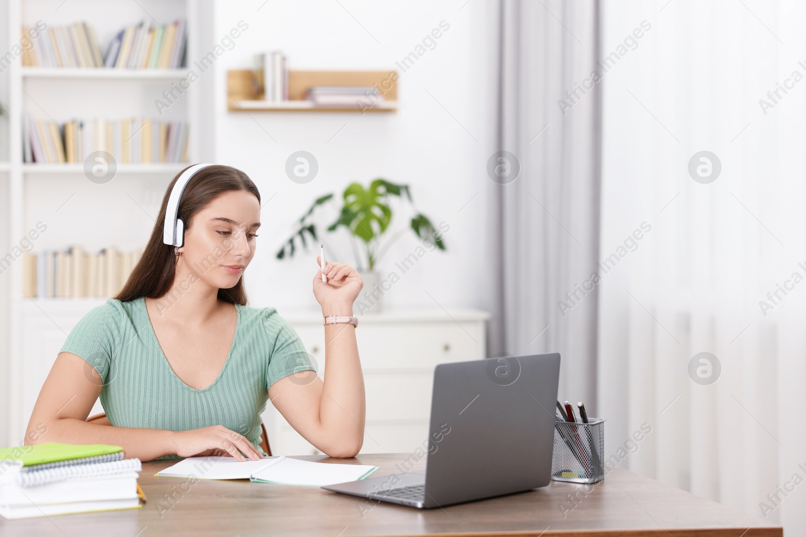 Photo of Student in headphones studying at wooden table indoors