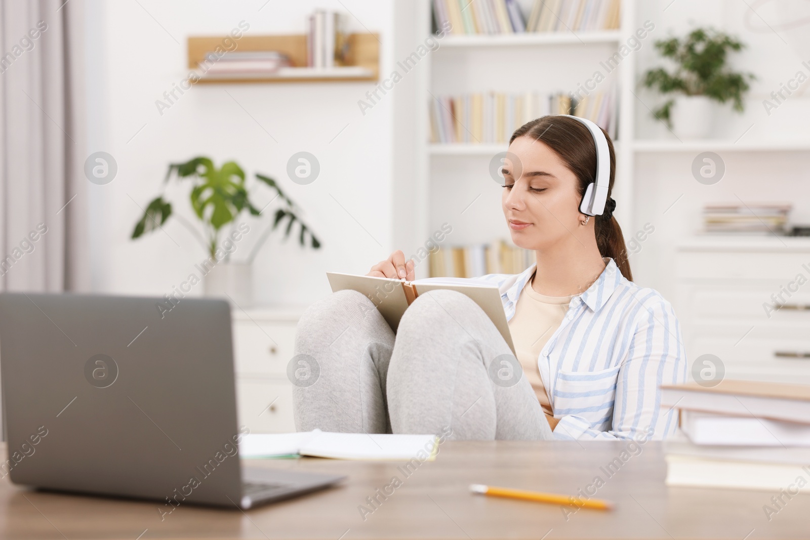 Photo of Student in headphones taking notes while studying indoors