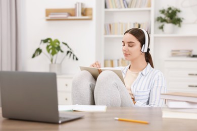 Student in headphones taking notes while studying indoors