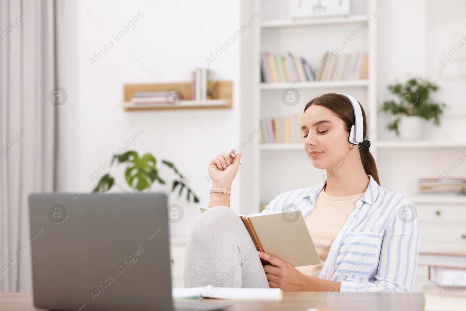 Photo of Student in headphones holding notebook and studying indoors