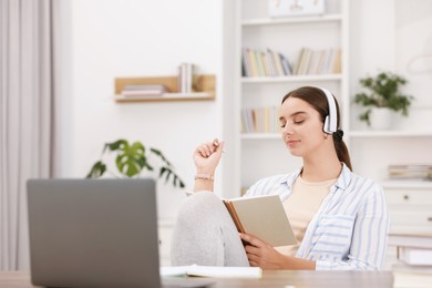 Photo of Student in headphones holding notebook and studying indoors