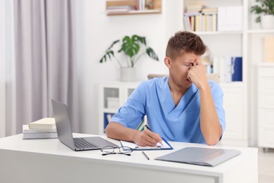 Medical student taking notes while studying at table indoors