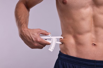 Photo of Man measuring body fat with caliper on grey background, closeup