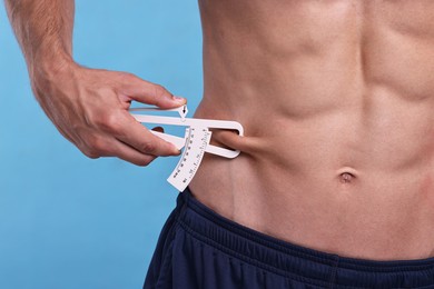 Photo of Man measuring body fat with caliper on light blue background, closeup