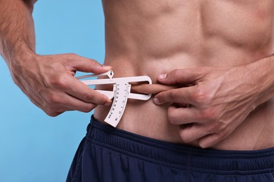 Photo of Man measuring body fat with caliper on light blue background, closeup