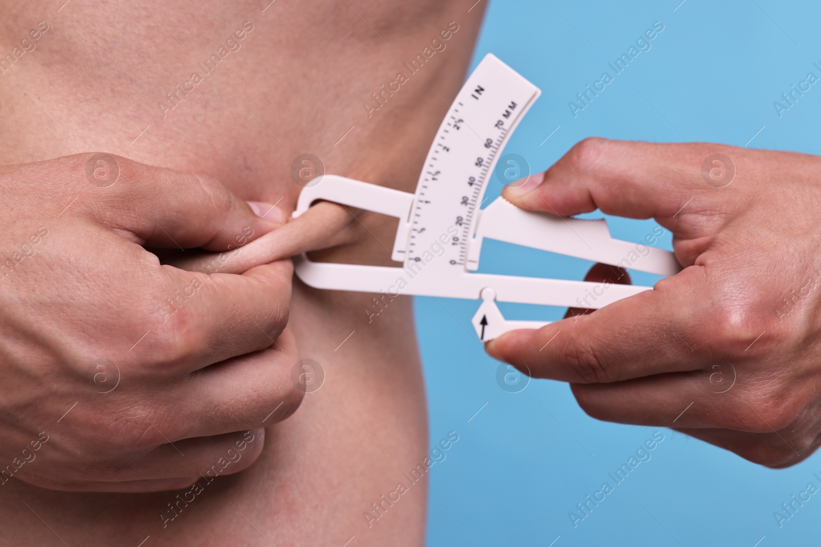 Photo of Man measuring body fat with caliper on light blue background, closeup