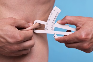 Photo of Man measuring body fat with caliper on light blue background, closeup