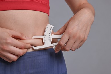 Photo of Woman measuring body fat with caliper on gray background, closeup