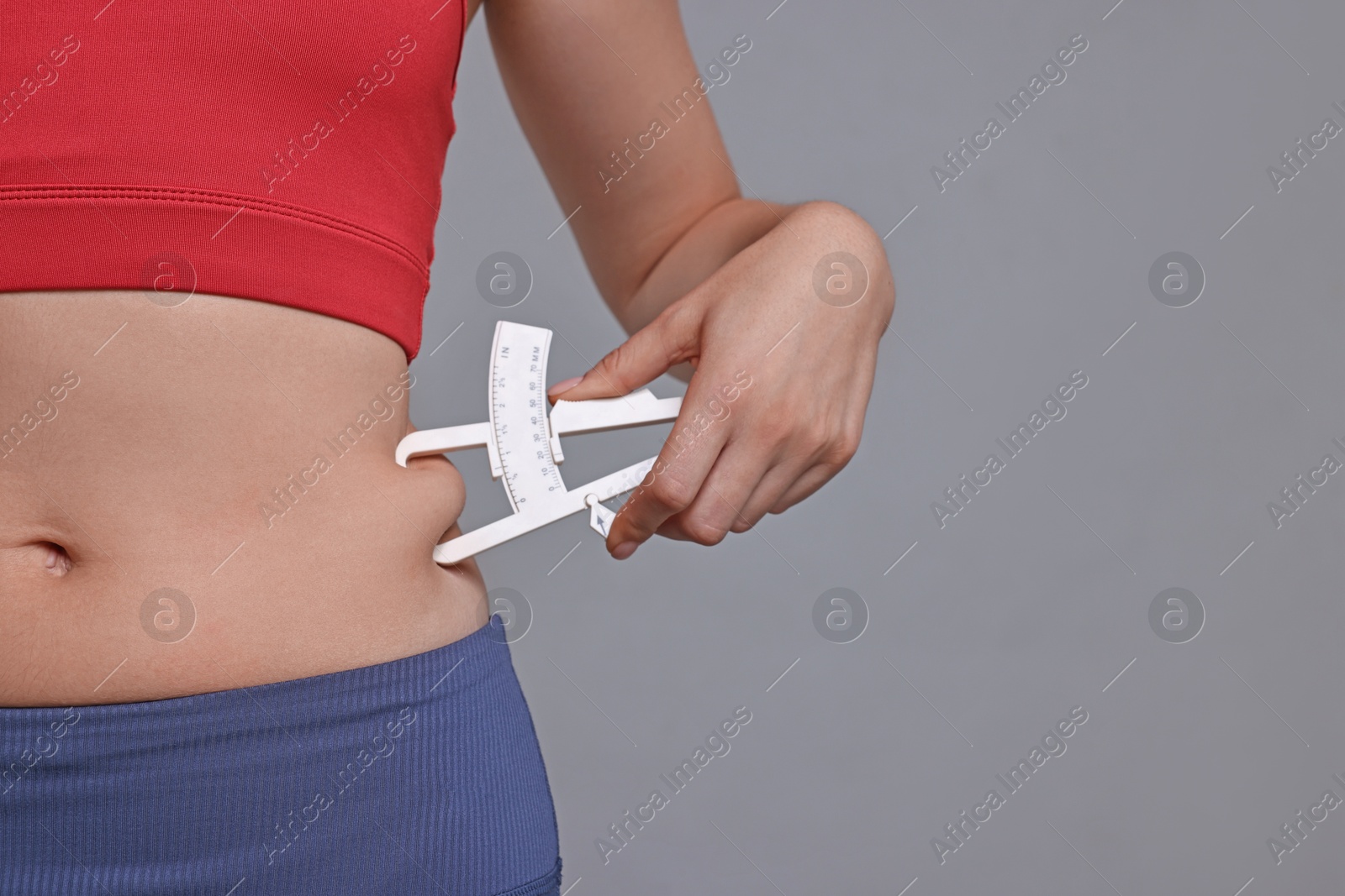 Photo of Woman measuring body fat with caliper on gray background, closeup. Space for text