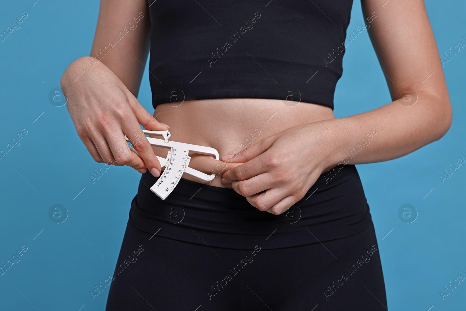 Photo of Woman measuring body fat with caliper on blue background, closeup