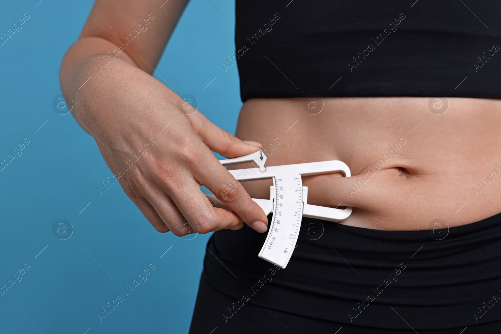 Photo of Woman measuring body fat with caliper on blue background, closeup