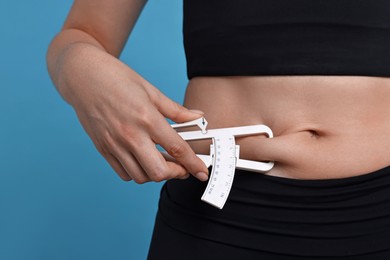 Photo of Woman measuring body fat with caliper on blue background, closeup