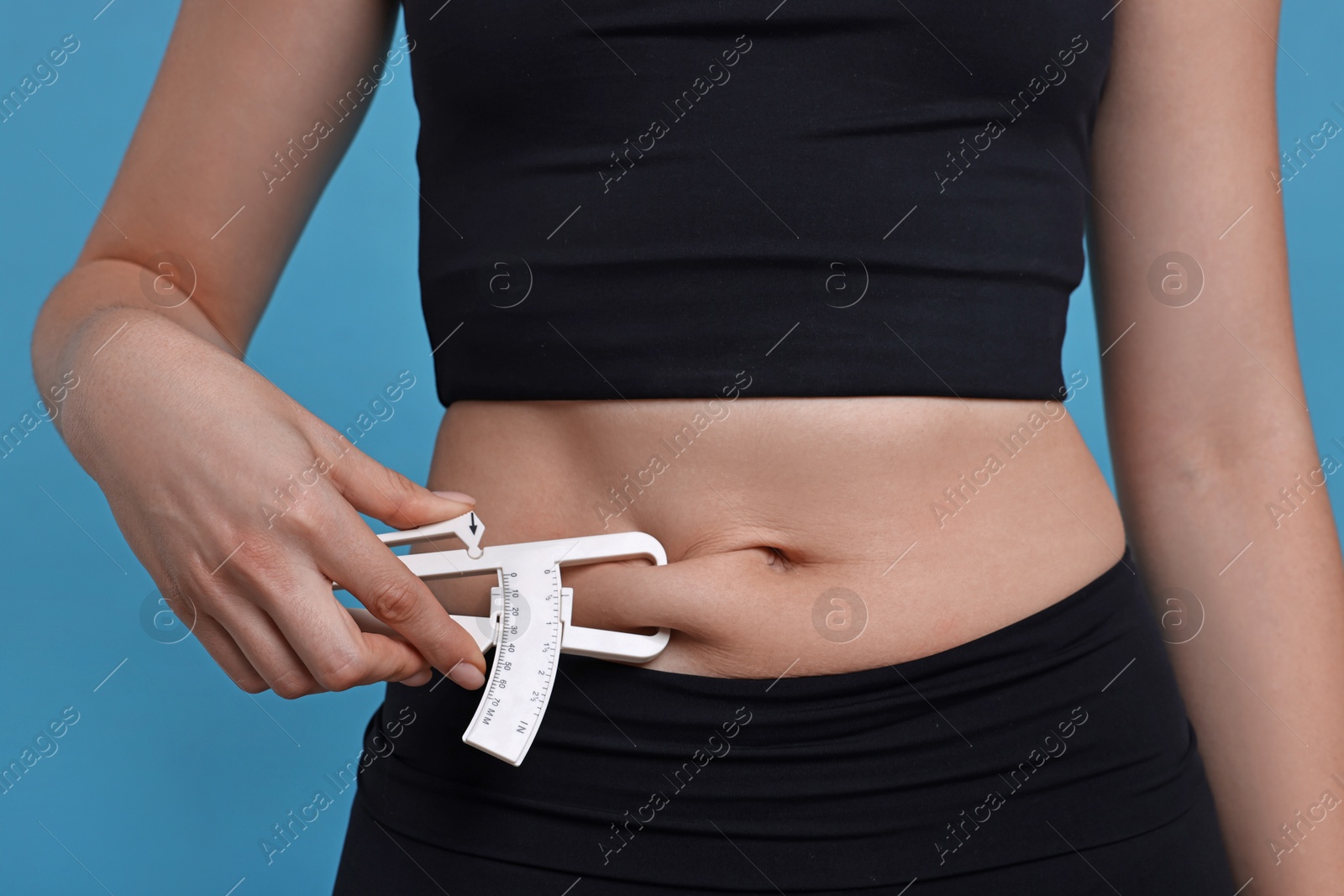 Photo of Woman measuring body fat with caliper on blue background, closeup