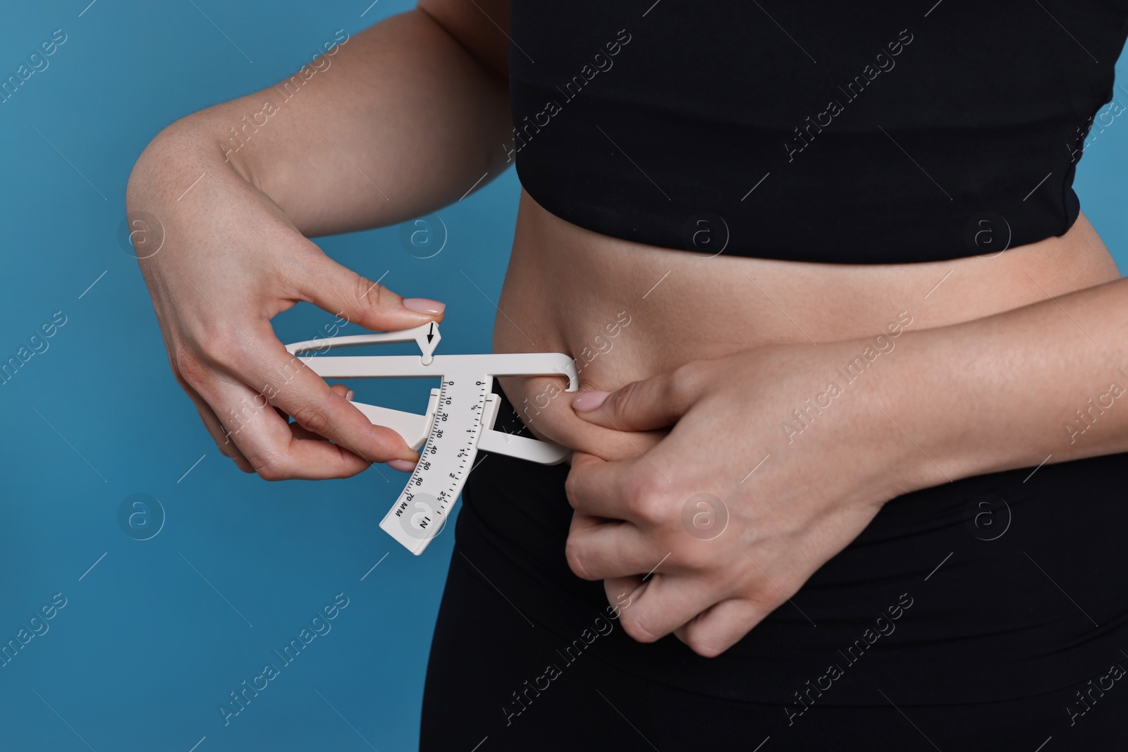 Photo of Woman measuring body fat with caliper on blue background, closeup