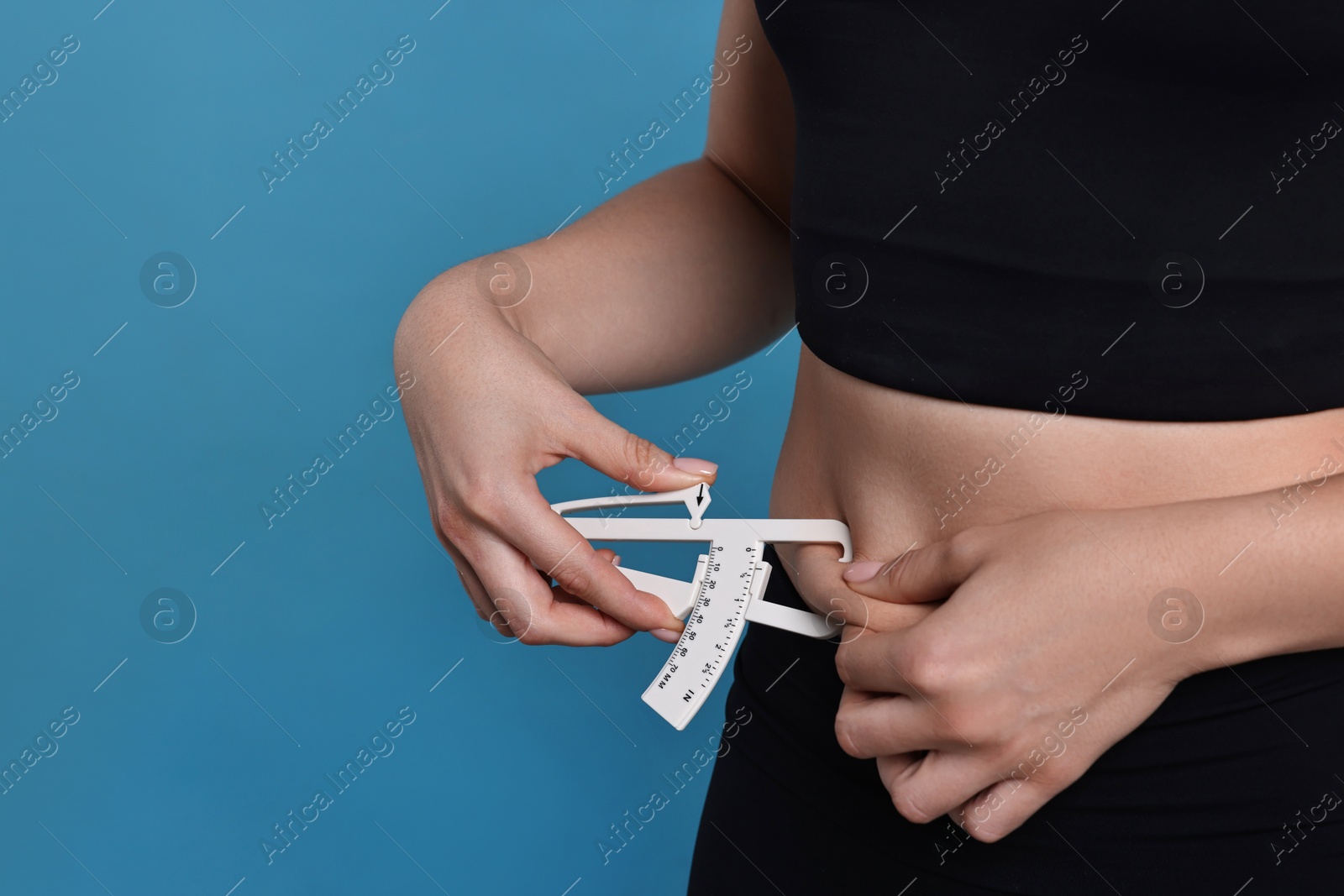 Photo of Woman measuring body fat with caliper on blue background, closeup