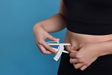 Photo of Woman measuring body fat with caliper on blue background, closeup