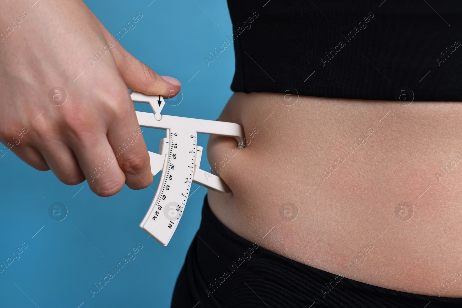 Photo of Woman measuring body fat with caliper on blue background, closeup