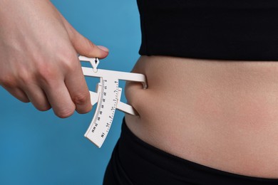 Photo of Woman measuring body fat with caliper on blue background, closeup