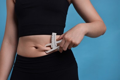 Photo of Woman measuring body fat with caliper on blue background, closeup