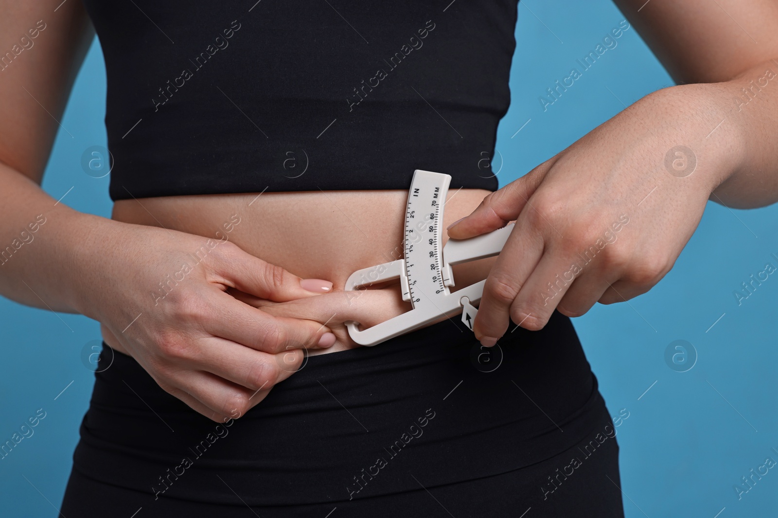 Photo of Woman measuring body fat with caliper on blue background, closeup