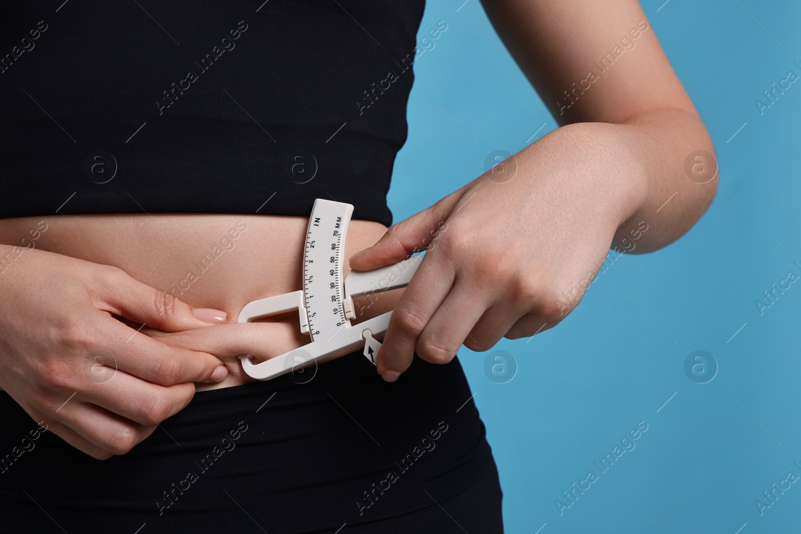 Photo of Woman measuring body fat with caliper on blue background, closeup