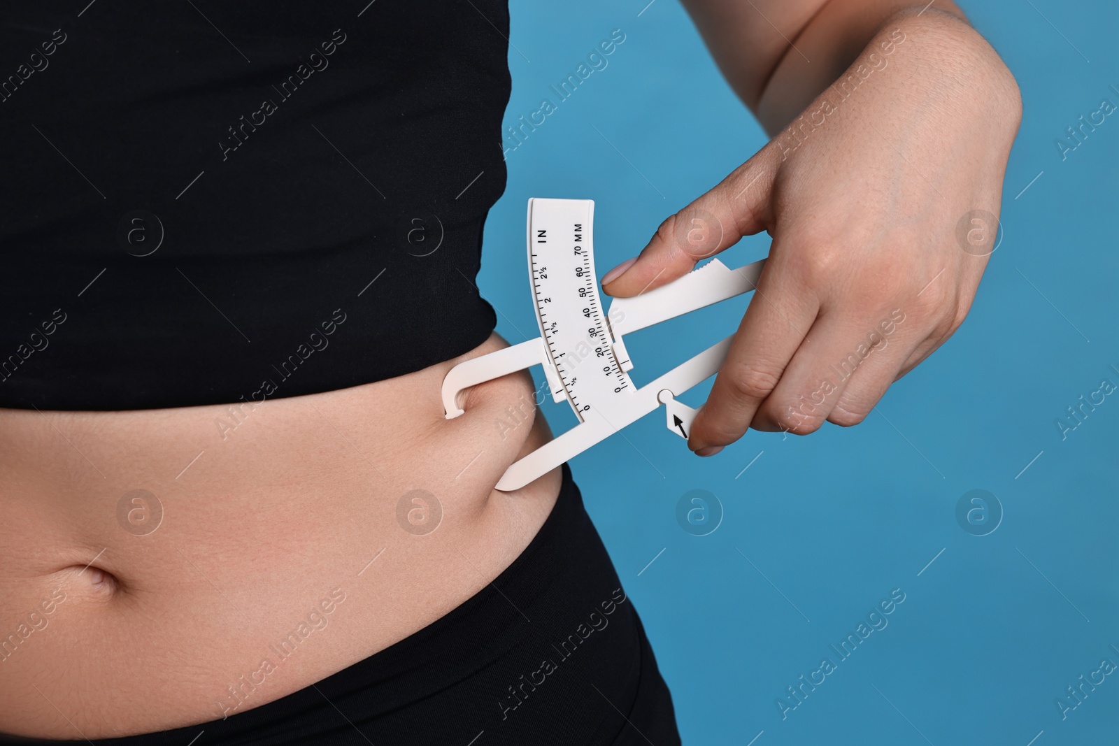 Photo of Woman measuring body fat with caliper on blue background, closeup