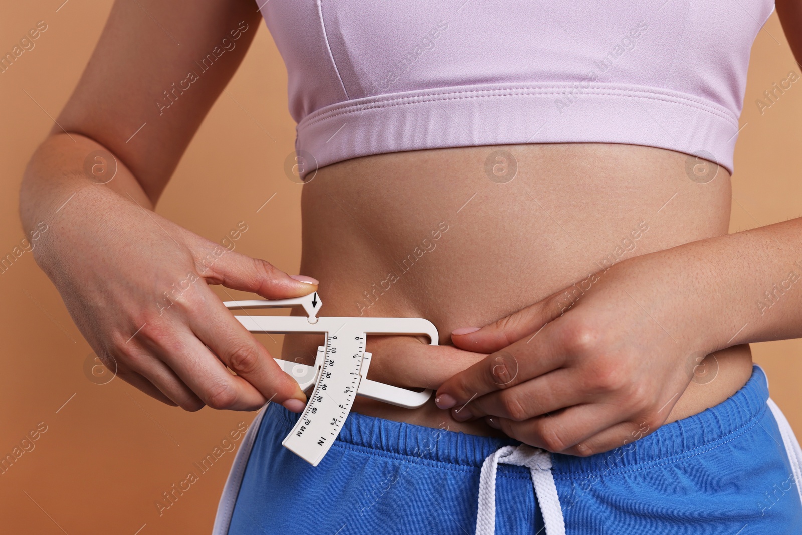 Photo of Woman measuring body fat with caliper on beige background, closeup