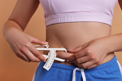 Photo of Woman measuring body fat with caliper on beige background, closeup