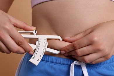 Photo of Woman measuring body fat with caliper on beige background, closeup