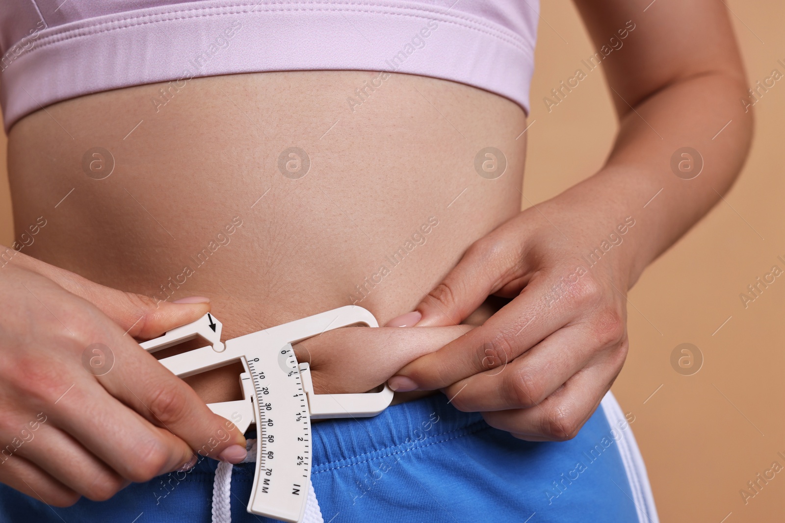 Photo of Woman measuring body fat with caliper on beige background, closeup